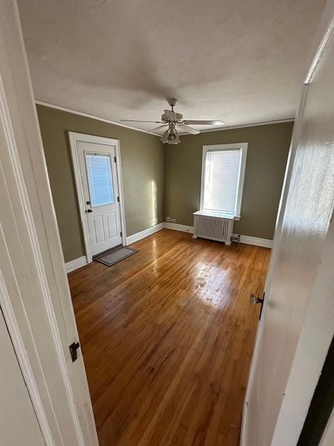 empty room with a ceiling fan, radiator heating unit, baseboards, and wood finished floors