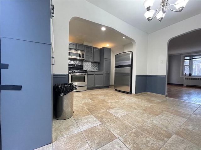 kitchen featuring appliances with stainless steel finishes, light wood-type flooring, radiator, gray cabinetry, and a chandelier