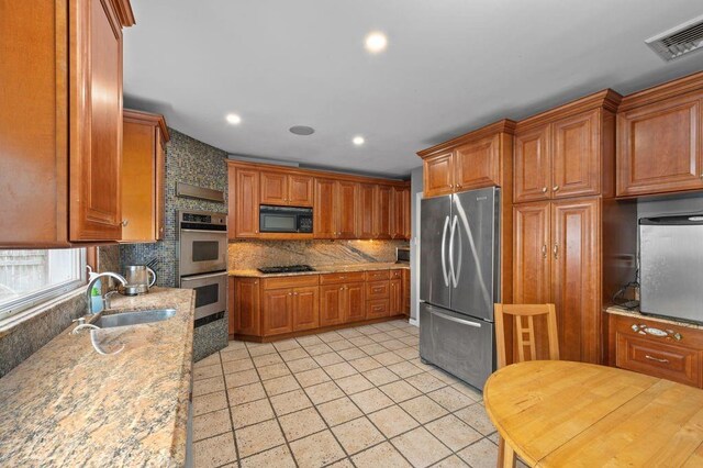 kitchen featuring light stone countertops, sink, decorative backsplash, light tile patterned floors, and black appliances