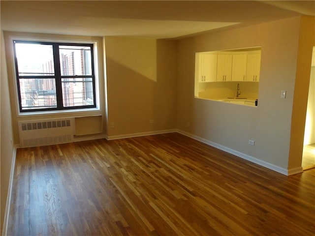 spare room with baseboards, a sink, radiator, and dark wood finished floors
