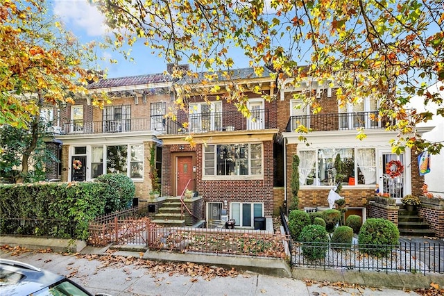 view of front facade featuring a fenced front yard, brick siding, and a balcony