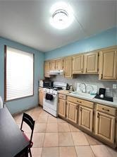 kitchen featuring light brown cabinetry, white range oven, sink, and light tile patterned flooring