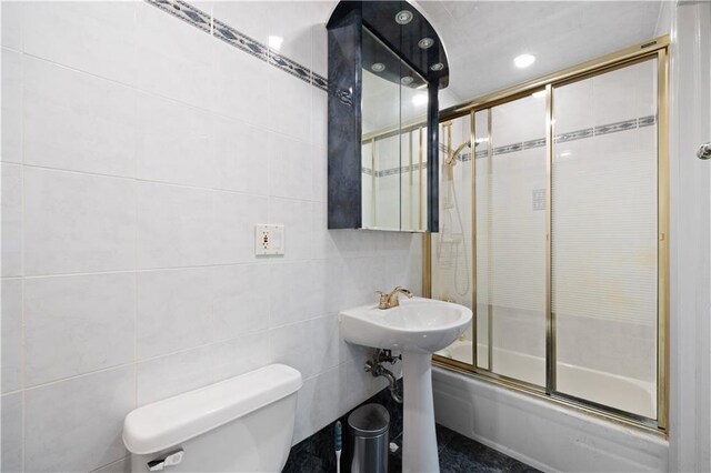 bathroom featuring bath / shower combo with glass door, tile walls, and toilet