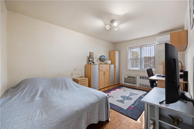 bedroom with light parquet flooring, radiator heating unit, and a wall unit AC