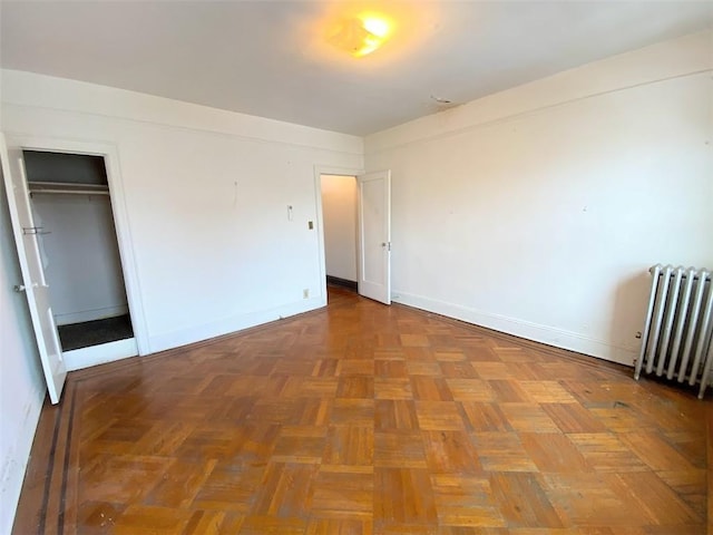 unfurnished bedroom with parquet floors, radiator heating unit, and a closet