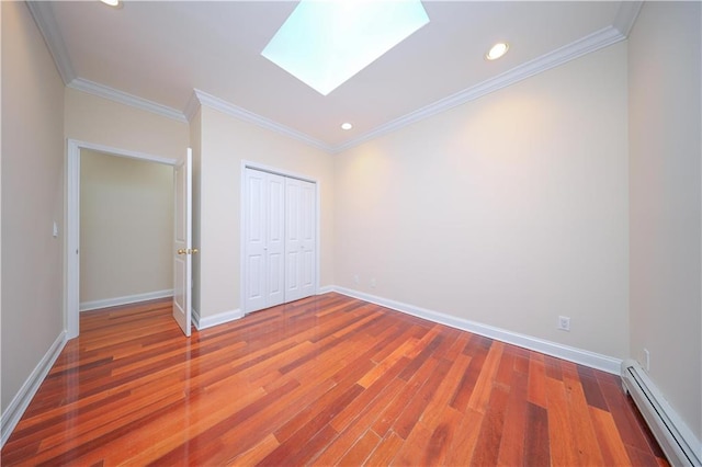 unfurnished bedroom featuring baseboard heating, hardwood / wood-style floors, a skylight, ornamental molding, and a closet