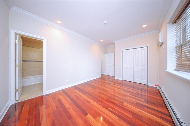 unfurnished bedroom featuring ensuite bath, a baseboard heating unit, wood-type flooring, ornamental molding, and a closet