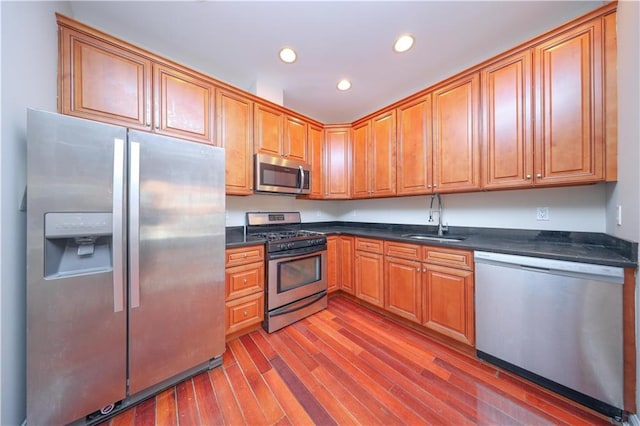 kitchen featuring wood finished floors, recessed lighting, a sink, stainless steel appliances, and dark countertops