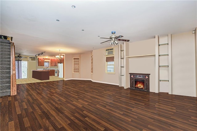 unfurnished living room featuring ceiling fan with notable chandelier, dark wood-type flooring, and a healthy amount of sunlight