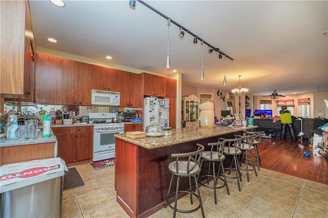 kitchen with decorative light fixtures, light hardwood / wood-style flooring, a breakfast bar area, white appliances, and ceiling fan with notable chandelier