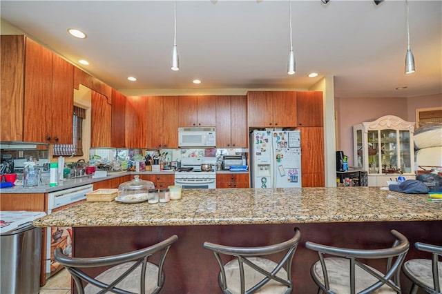 kitchen with white appliances, sink, light stone counters, and hanging light fixtures