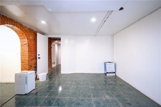 tiled spare room featuring arched walkways, brick wall, and recessed lighting