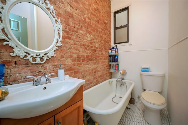 bathroom featuring a bathing tub, vanity, toilet, and brick wall