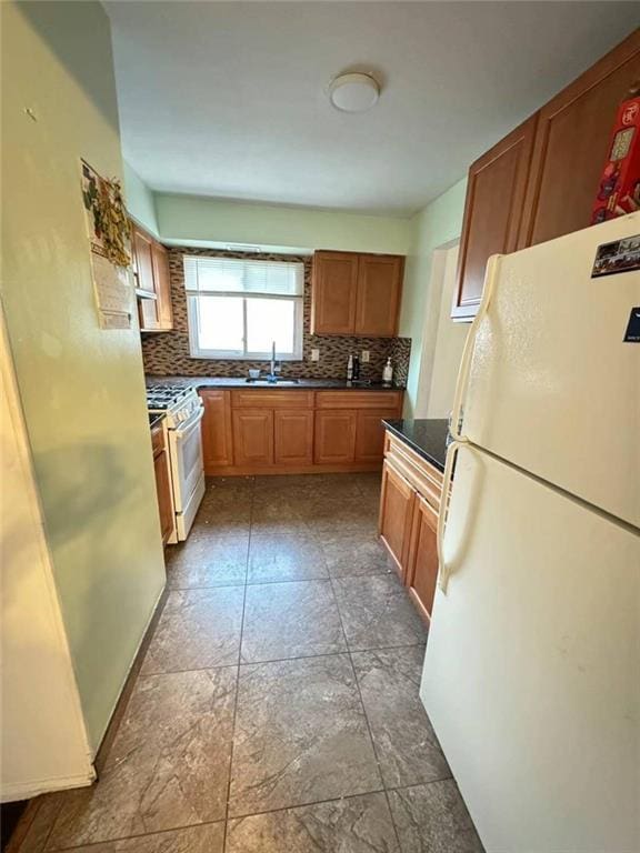 kitchen featuring white appliances, a sink, decorative backsplash, brown cabinets, and dark countertops