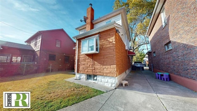 back of property with driveway, stone siding, a lawn, and a chimney