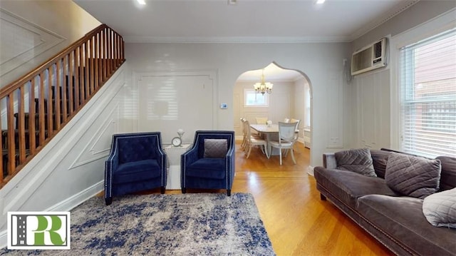 living area featuring ornamental molding, wood finished floors, a wall mounted air conditioner, arched walkways, and a notable chandelier