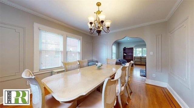 dining space featuring arched walkways, crown molding, a notable chandelier, light wood-type flooring, and baseboards