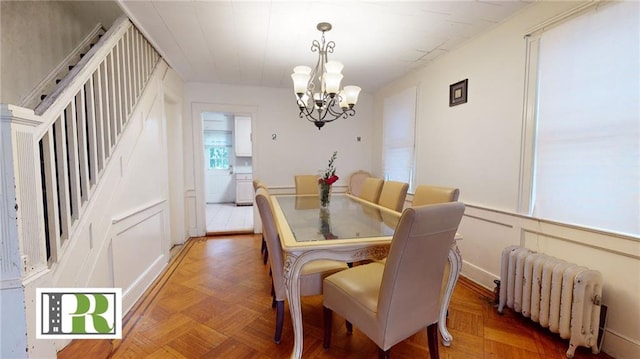 dining room featuring a chandelier, radiator heating unit, and stairs