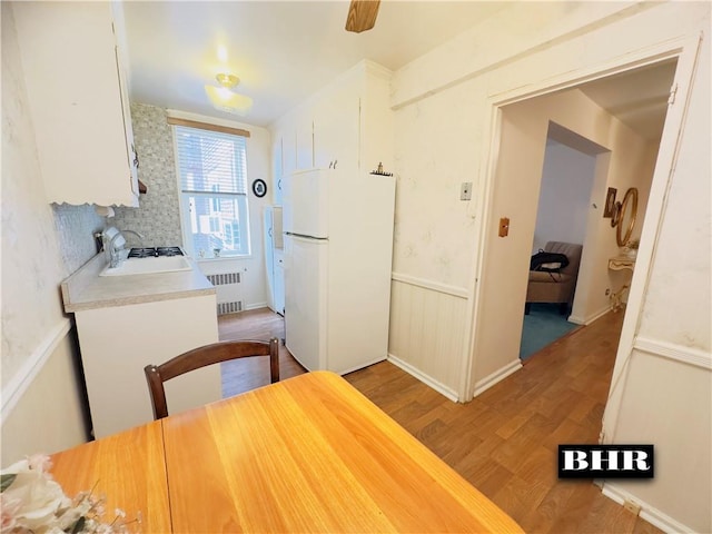 kitchen with backsplash, radiator, hardwood / wood-style flooring, white fridge, and white cabinetry