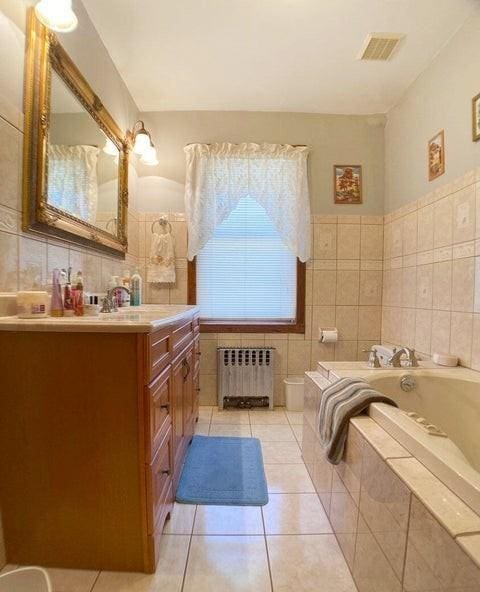 bathroom featuring tile patterned floors, radiator, tile walls, tiled tub, and vanity