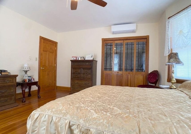 bedroom with a wall mounted AC, multiple windows, wood-type flooring, and ceiling fan