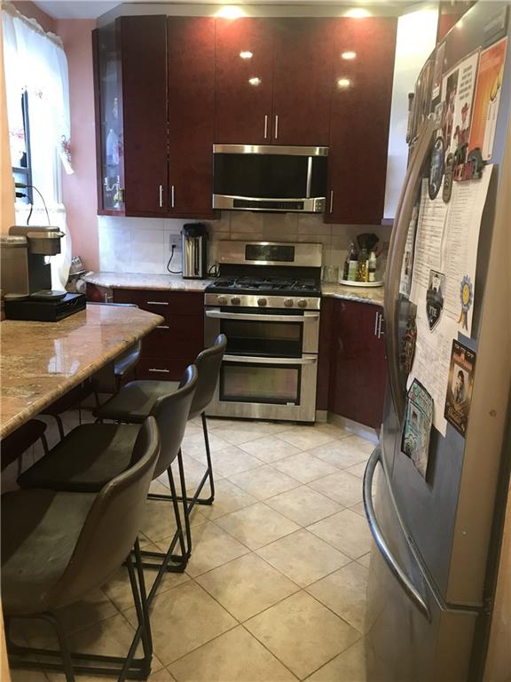 kitchen featuring light tile patterned flooring, appliances with stainless steel finishes, a breakfast bar, tasteful backsplash, and light stone counters