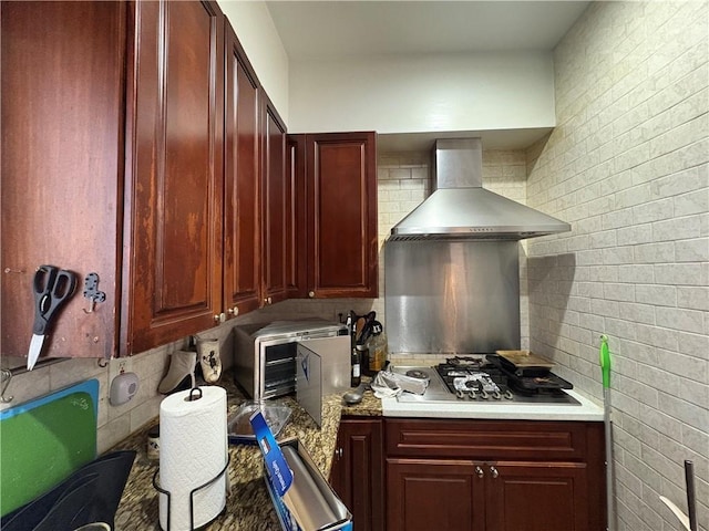 kitchen featuring backsplash, stainless steel gas stovetop, wall chimney exhaust hood, and brick wall