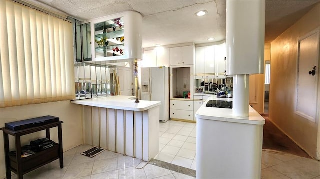 kitchen with light tile patterned floors, white cabinetry, white fridge with ice dispenser, and kitchen peninsula