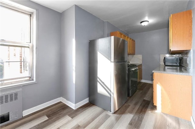 kitchen featuring black range with gas stovetop, a healthy amount of sunlight, stainless steel fridge, and radiator heating unit