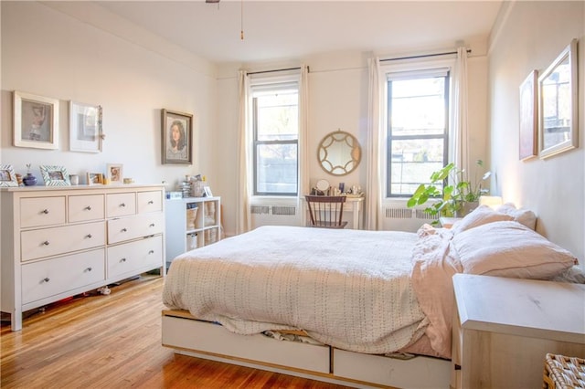 bedroom featuring multiple windows, radiator heating unit, and light wood-type flooring