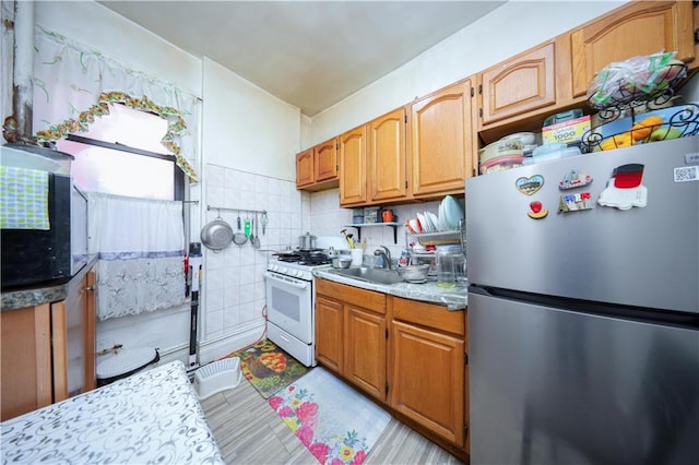 kitchen with white range with gas stovetop, sink, backsplash, and stainless steel refrigerator