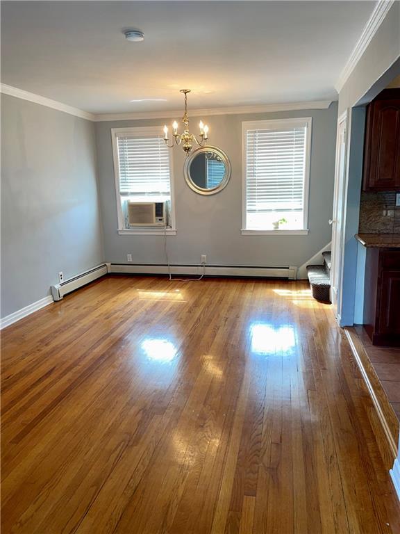 unfurnished dining area featuring an inviting chandelier, ornamental molding, light hardwood / wood-style floors, and baseboard heating