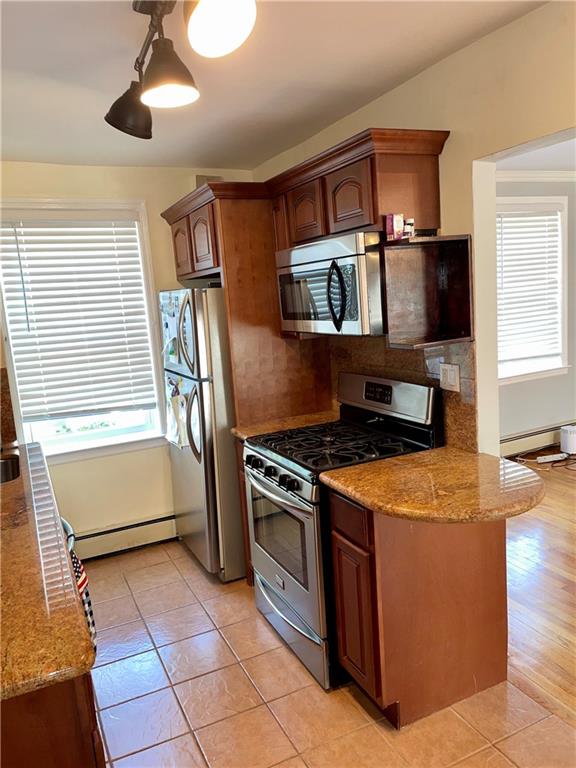 kitchen with light tile patterned floors, stainless steel appliances, a healthy amount of sunlight, and a baseboard heating unit