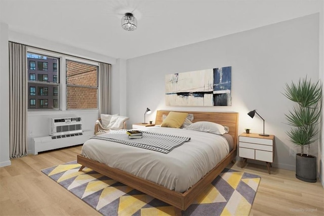 bedroom with baseboard heating, a wall mounted air conditioner, and light hardwood / wood-style floors