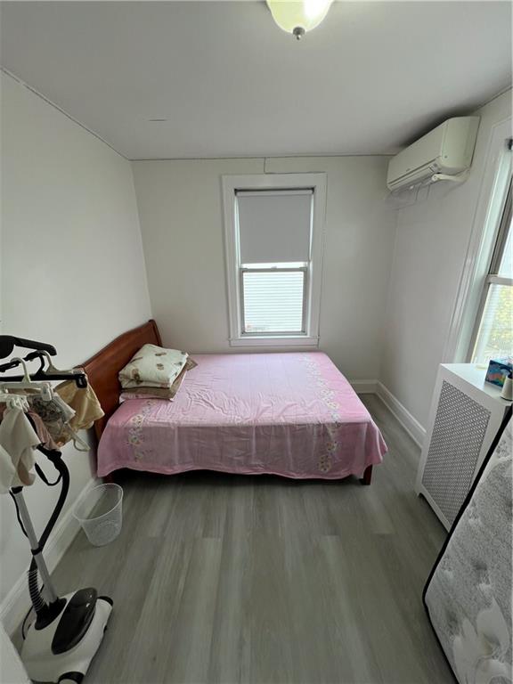 bedroom with wood-type flooring, multiple windows, a wall mounted air conditioner, and radiator