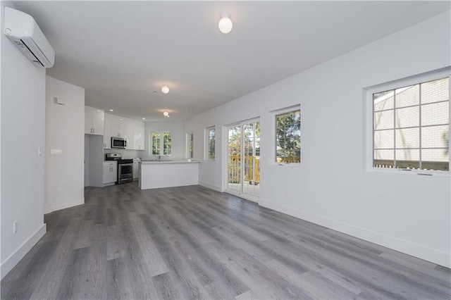 unfurnished living room featuring wood-type flooring and a wall mounted air conditioner