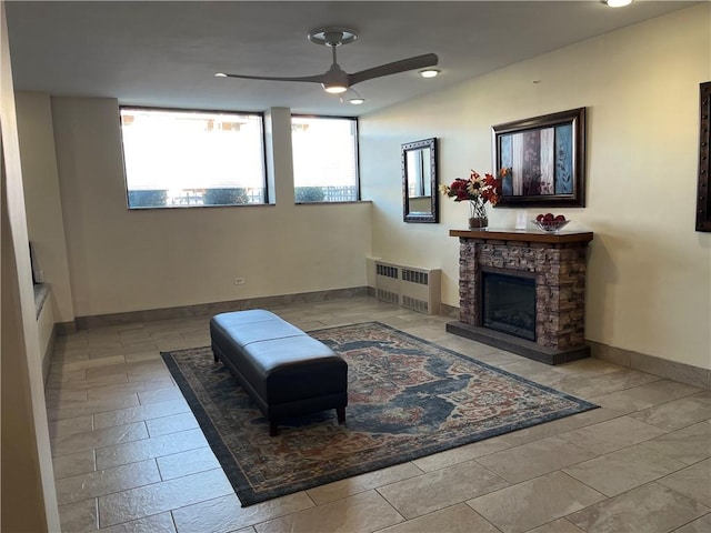 sitting room featuring ceiling fan, a stone fireplace, a healthy amount of sunlight, and radiator