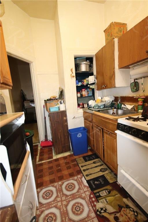 kitchen featuring white range with gas cooktop, dark floors, brown cabinets, and a sink