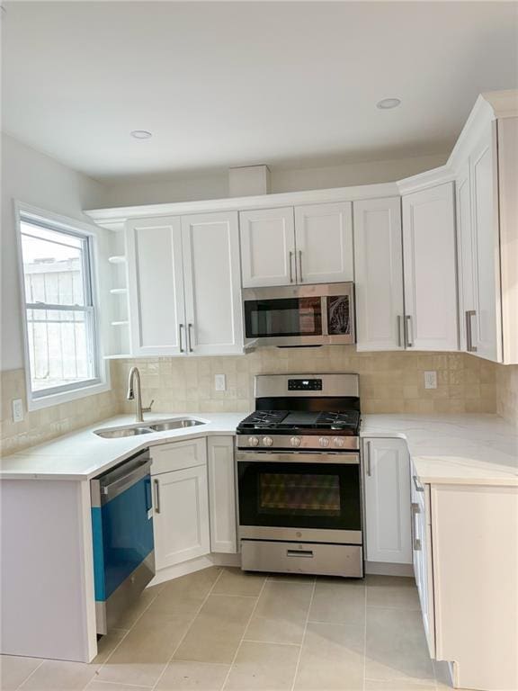 kitchen with appliances with stainless steel finishes, sink, white cabinetry, and light tile patterned flooring