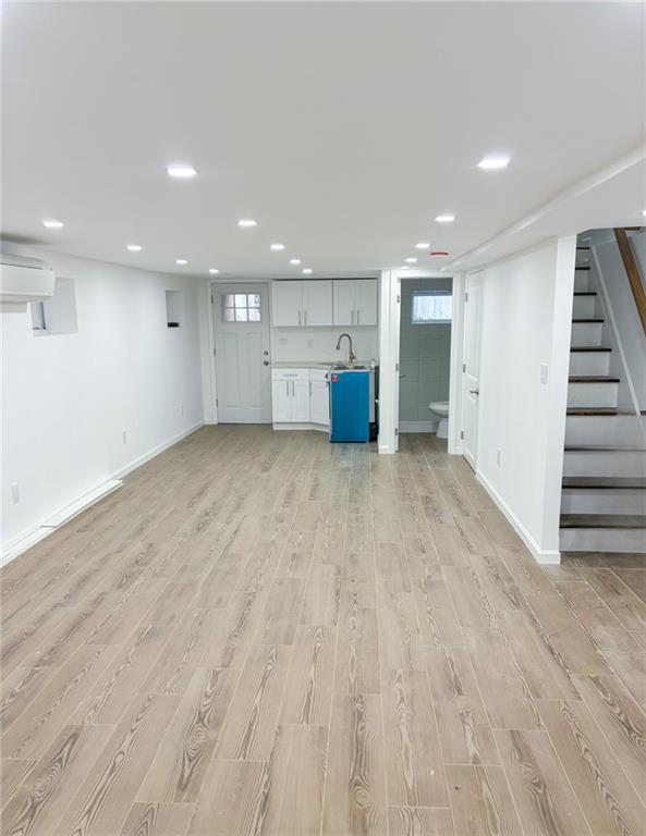 basement with a wall mounted AC, light hardwood / wood-style flooring, and sink