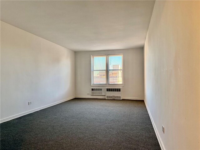 unfurnished room featuring radiator heating unit and dark carpet