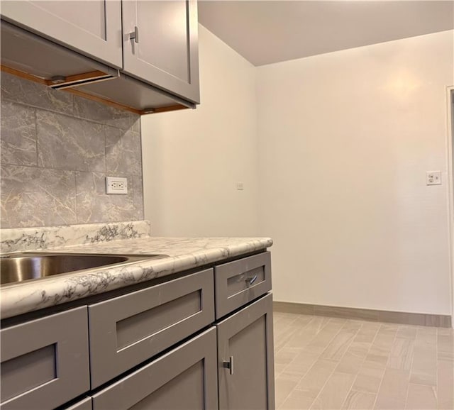 kitchen with light stone counters, backsplash, and gray cabinets