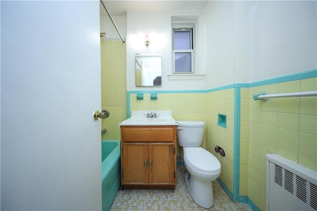 full bathroom featuring radiator, tile walls, vanity, toilet, and washtub / shower combination