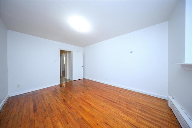 unfurnished room featuring hardwood / wood-style floors and a baseboard heating unit