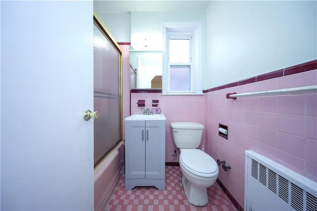 full bathroom featuring enclosed tub / shower combo, tile walls, radiator heating unit, vanity, and toilet