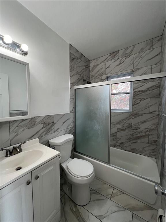 full bathroom featuring toilet, vanity, bath / shower combo with glass door, and tile walls