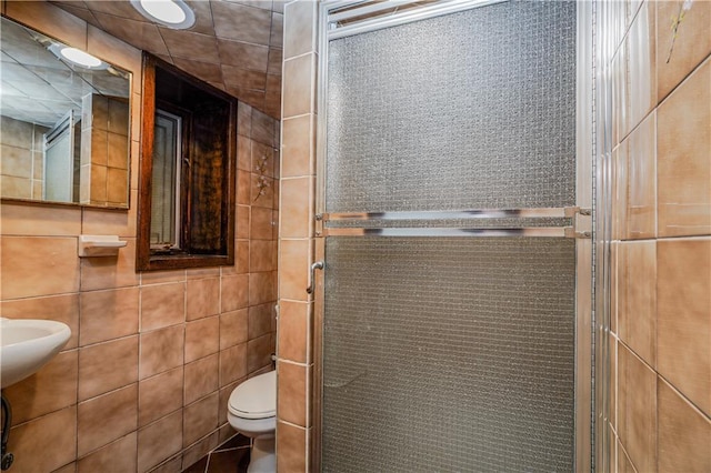 bathroom featuring a shower with shower door, tile walls, and toilet