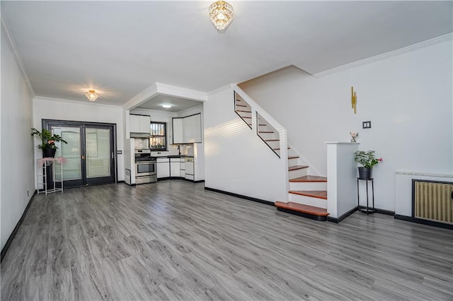 unfurnished living room with stairs, radiator heating unit, wood finished floors, and ornamental molding