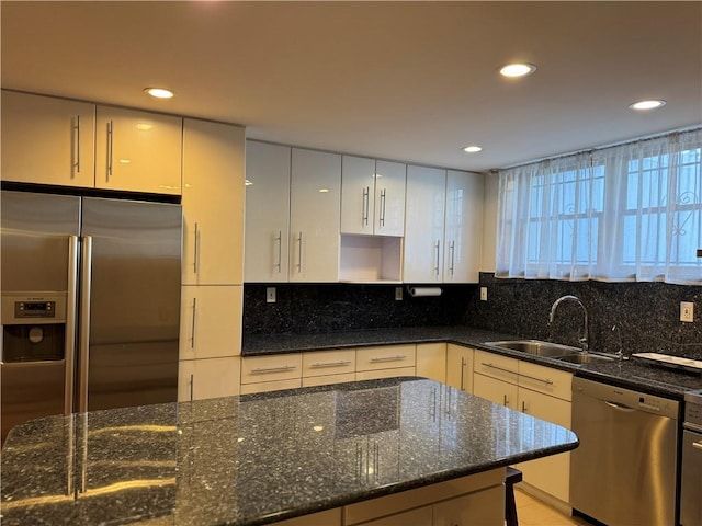 kitchen with stainless steel appliances, sink, decorative backsplash, and dark stone countertops