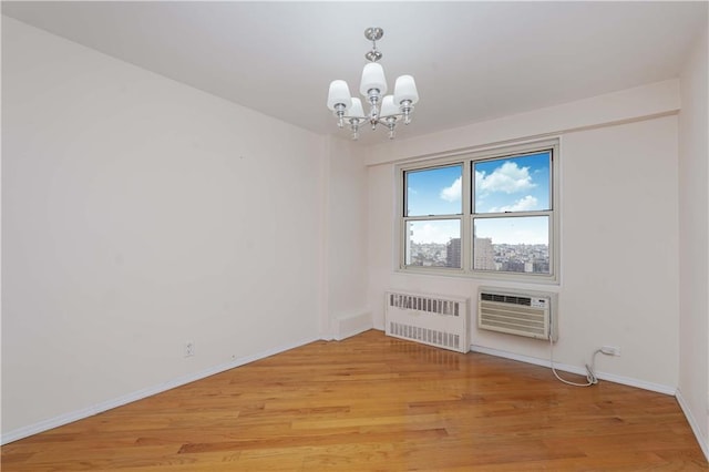 unfurnished room featuring baseboards, light wood finished floors, a wall mounted AC, radiator heating unit, and a chandelier